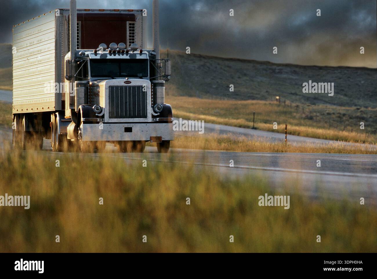 Un grande camion guida su una strada aperta circondata da erba e colline durante la luce delle ore d'oro Foto Stock