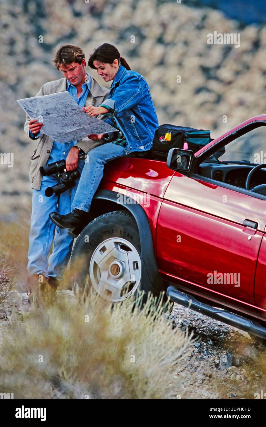 Due persone guardano una mappa mentre sono sedute su un'auto rossa in un'area desertica durante il giorno Foto Stock