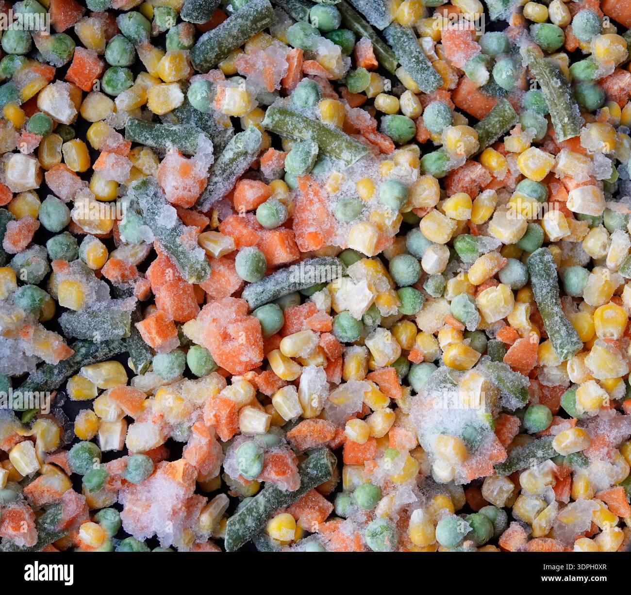 Le verdure miste congelate vengono distribuite su una superficie pulita della cucina. La miscela contiene piselli, carote, mais e fagioli verdi. Sembra fresco e pronto a farlo Foto Stock
