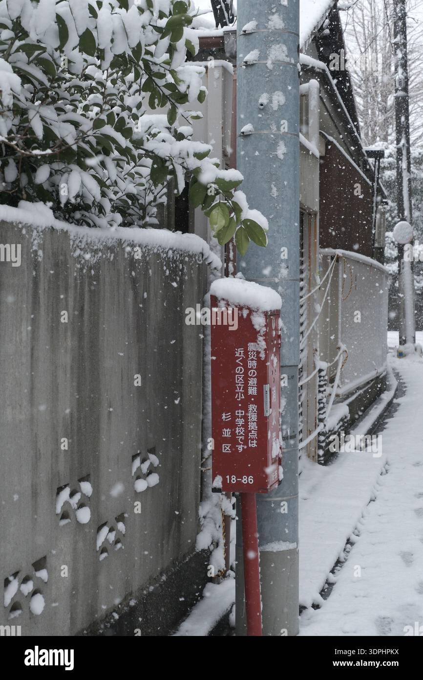 Una bacheca rossa di informazioni di emergenza coperta di neve lungo uno stretto vicolo residenziale a Suginami, Tokyo Foto Stock