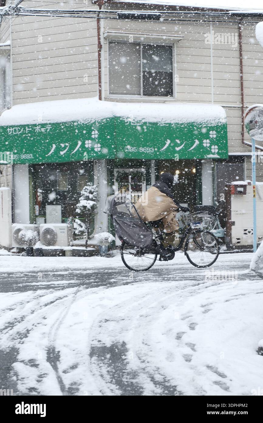 Un ciclista passa davanti a un negozio di tende verdi durante una forte tempesta di neve a Tokyo Foto Stock