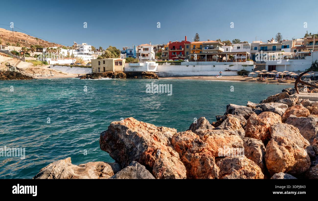 Panormos, Creta, Grecia - 9 settembre 2025: Vista costiera del villaggio di Panormos con porto, case sul mare e ombrelloni lungo il Mediterraneo Foto Stock