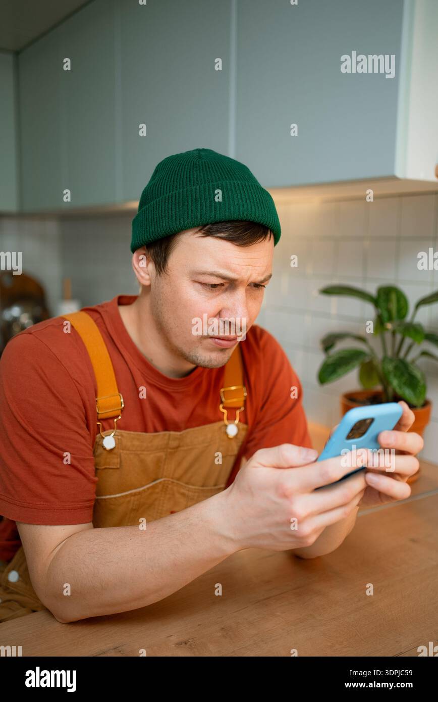 Uomo che legge cattive notizie su uno smartphone, che mostra un'espressione facciale angosciata a causa di informazioni allarmanti sui tagli di posti di lavoro, sulla riduzione dei salari e sull'incertezza economica che influenzano l'occupazione futura Foto Stock