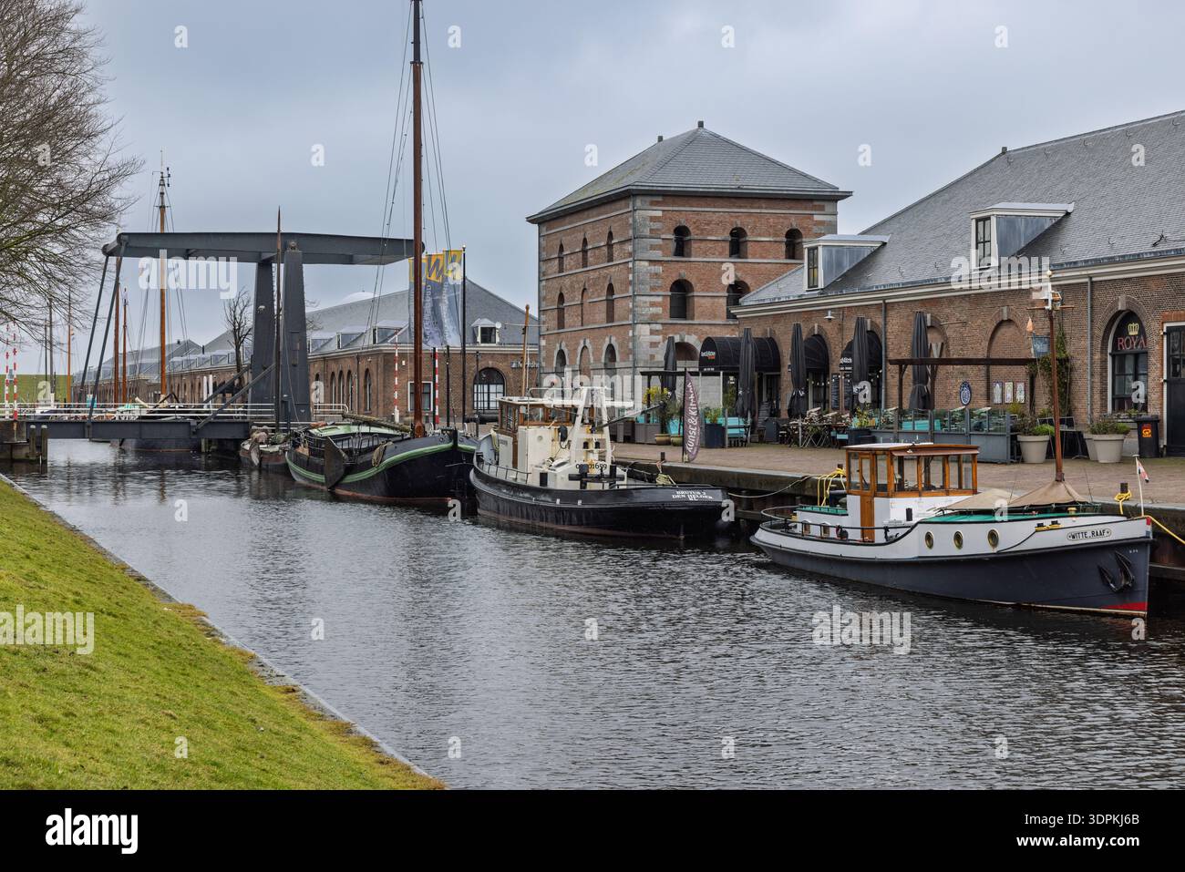 Vista panoramica di un canale a Willemsoord, Den Helder, caratterizzato da storici magazzini in mattoni, barche tradizionali e un classico ponte levatoio nero. Den Helder Foto Stock