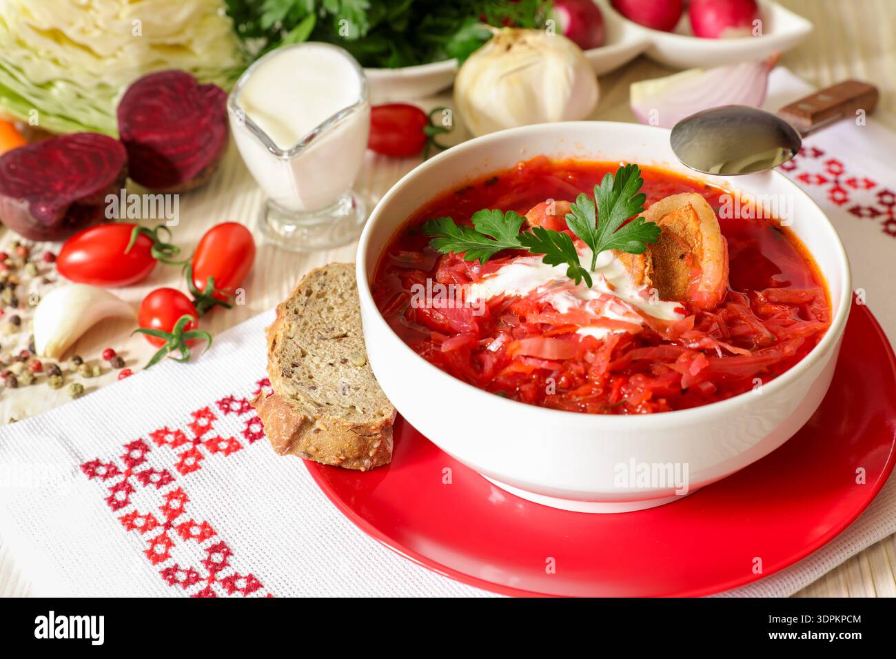 Ciotola bianca di zuppa tradizionale Ucraina borsch o zuppa di barbabietole vegetali su un tovagliolo bianco ricamato in stile ucraino accanto a ingredienti e spezie. Foto Stock