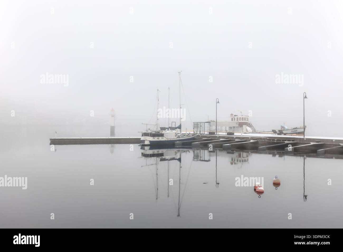Il lungofiume settentrionale è calmo e riflesso, le barche ormeggiate e il molo del porto si dissolvono nella fitta nebbia con alberi a specchio sull'acqua ferma per la serenità del porto locale Foto Stock