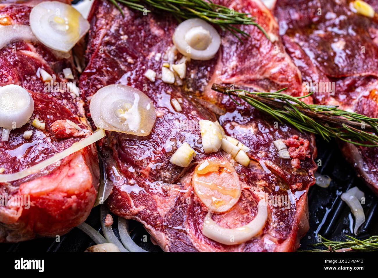 La carne di agnello cruda su una teglia da forno con cipolle, rosmarino, aglio, tagliata in bistecche è pronta per la frittura. Il processo di cottura dell'agnello. Foto di alta qualità Foto Stock