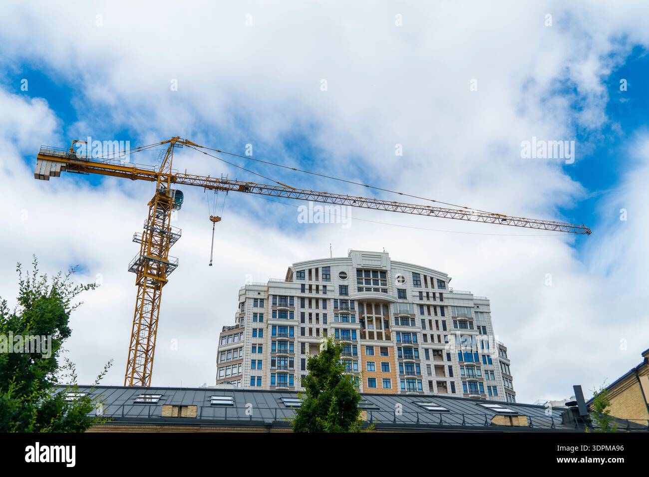 Grande gru a torre gialla che lavora su un cantiere di un alto edificio di appartamenti di lusso contro un cielo blu con nuvole. Sviluppo immobiliare Foto Stock