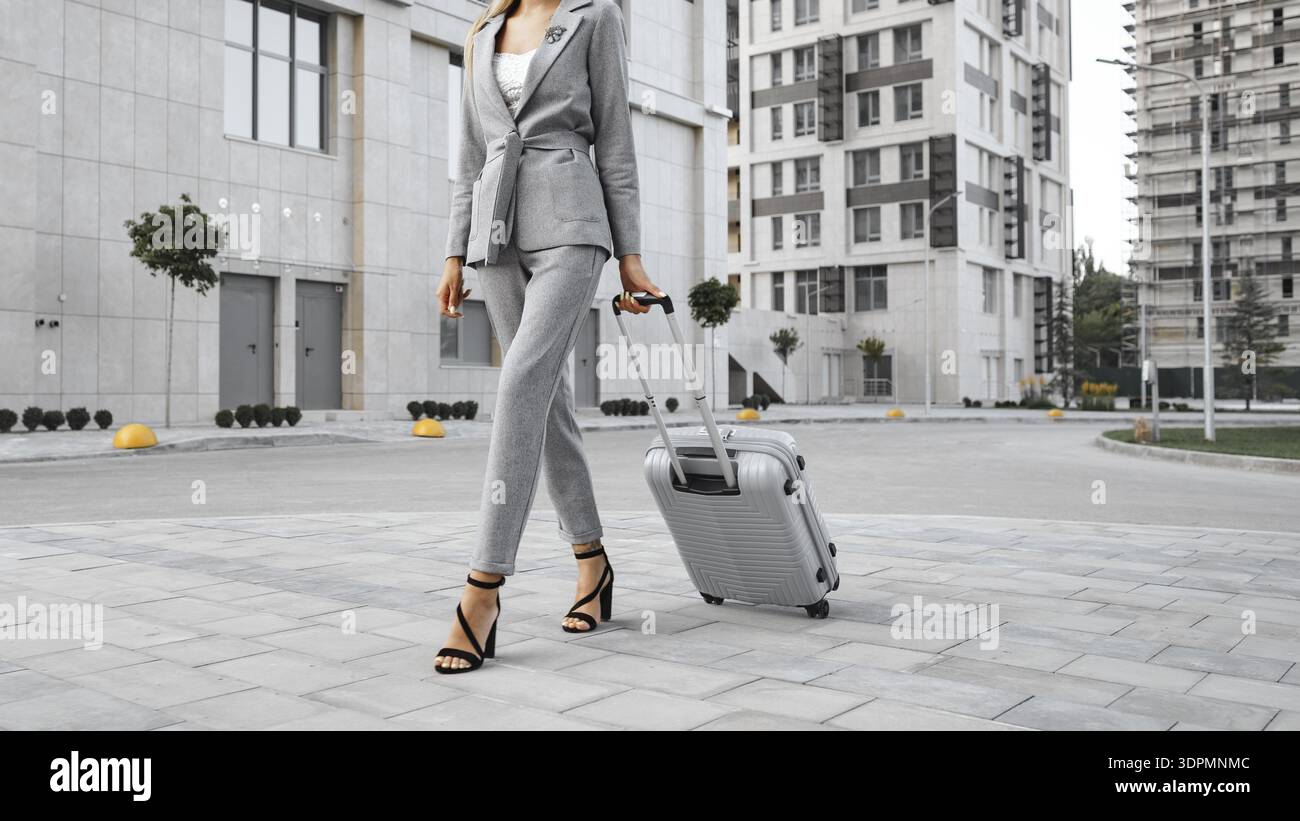 Donna che cammina con valigia in un ambiente urbano durante il giorno vicino a edifici moderni Foto Stock