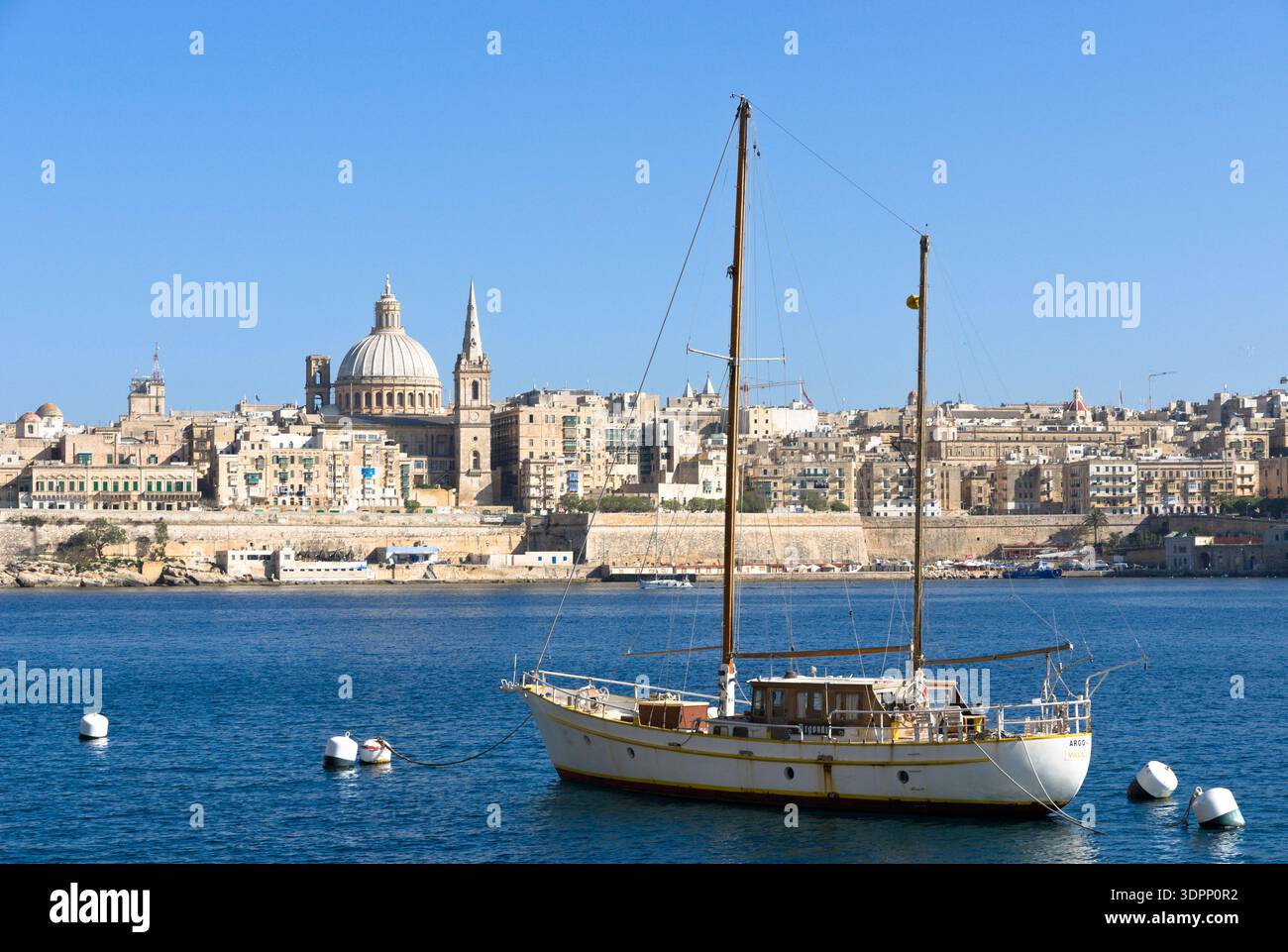 Una barca a vela ormeggiata nel porto di Marsamxett con l'iconica cupola della chiesa del Monte Carmelo e la pro-cattedrale di San Paolo nello skyline di Valletta, Malta. Foto Stock
