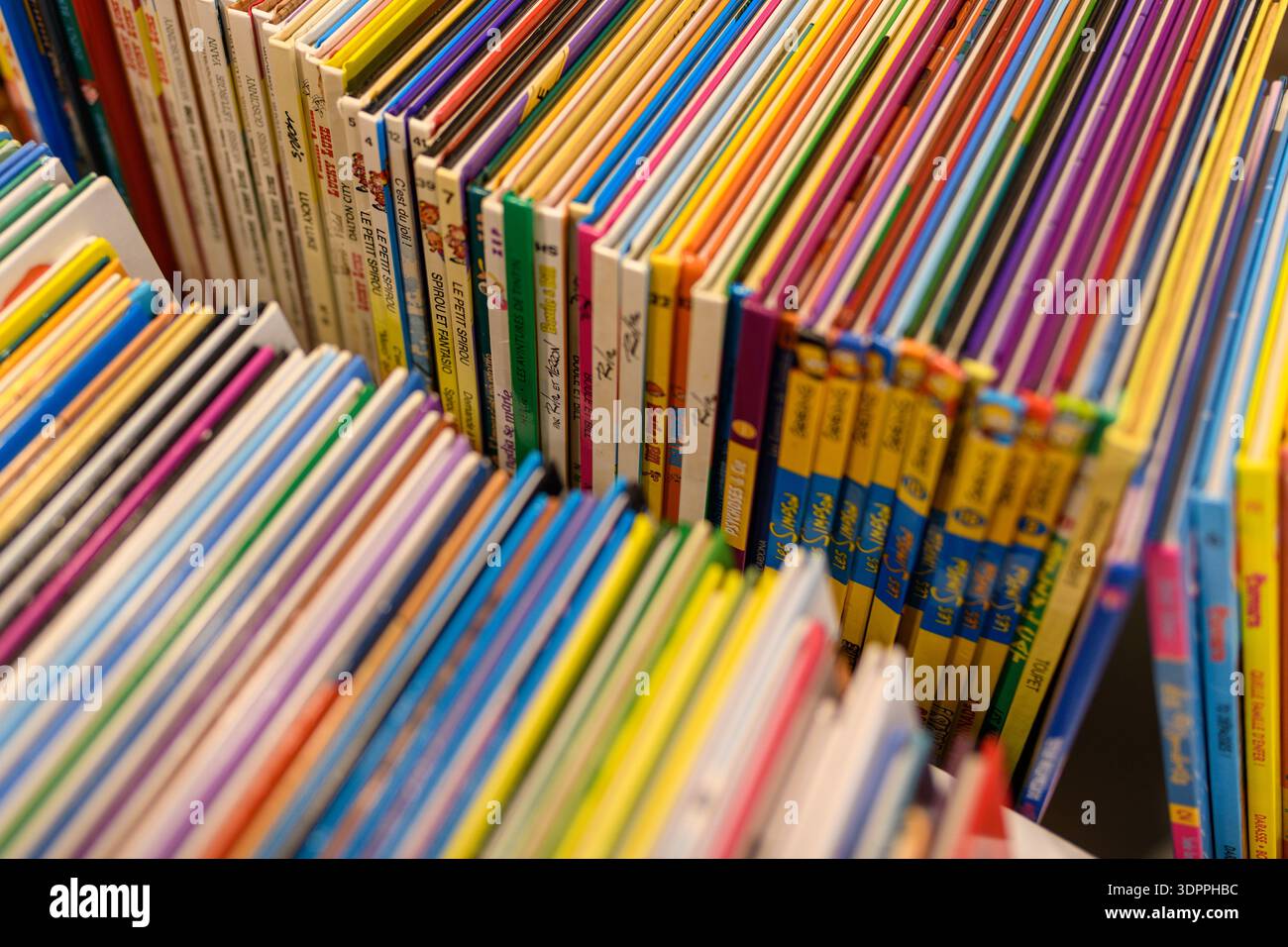 Posizione sconosciuta - 12 maggio 2021: Una vista ravvicinata mostra file di coloratissimi fumetti e libri per bambini disposti verticalmente su uno scaffale, con titoli francesi visibili e copertine illustrate. Foto Stock