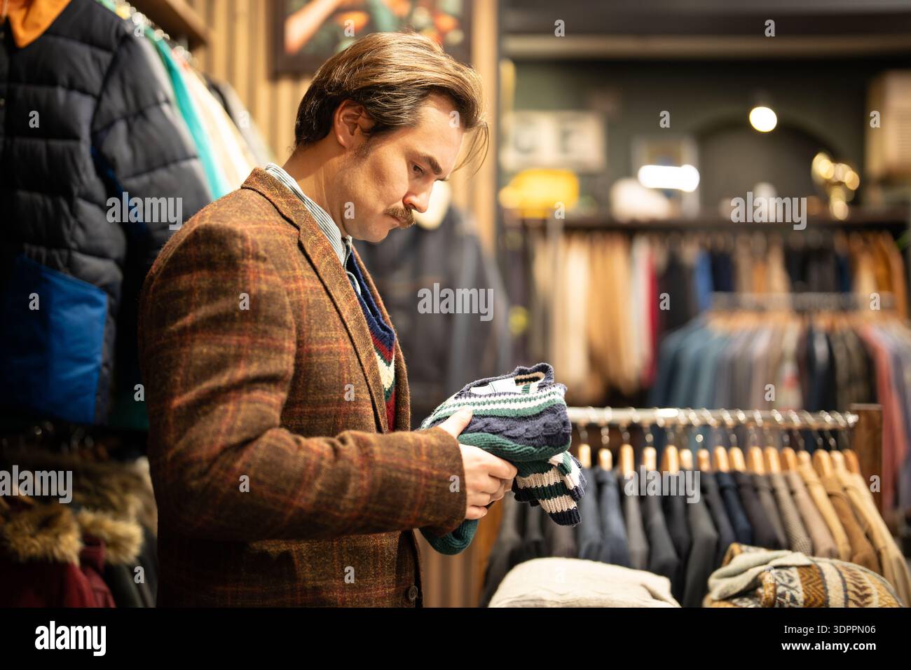 Elegante cliente che acquista abbigliamento usato in un negozio di abbigliamento vintage di seconda mano. Foto Stock