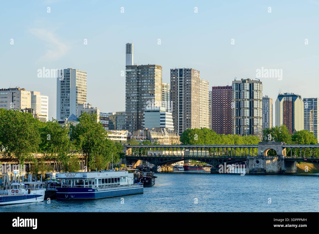 Parigi, Francia - 10 maggio 2022: Lo skyline del quartiere di Beaugrenelle, con i suoi alti e moderni edifici, è visibile dietro il ponte Pont de Bir-Hakeim che attraversa la Senna, con barche ormeggiate e alberi verdi lungo la riva del fiume sotto la luce del sole. Foto Stock