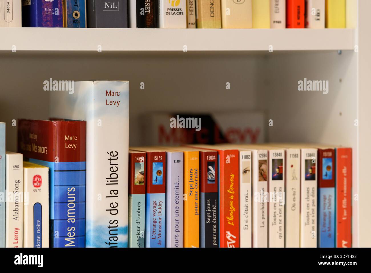 Posizione sconosciuta - 12 maggio 2021: Una vista ravvicinata di libri francesi, tra cui diversi di Marc Levy, disposti in verticale e orizzontalmente su una libreria bianca con titoli e spine visibili. Foto Stock