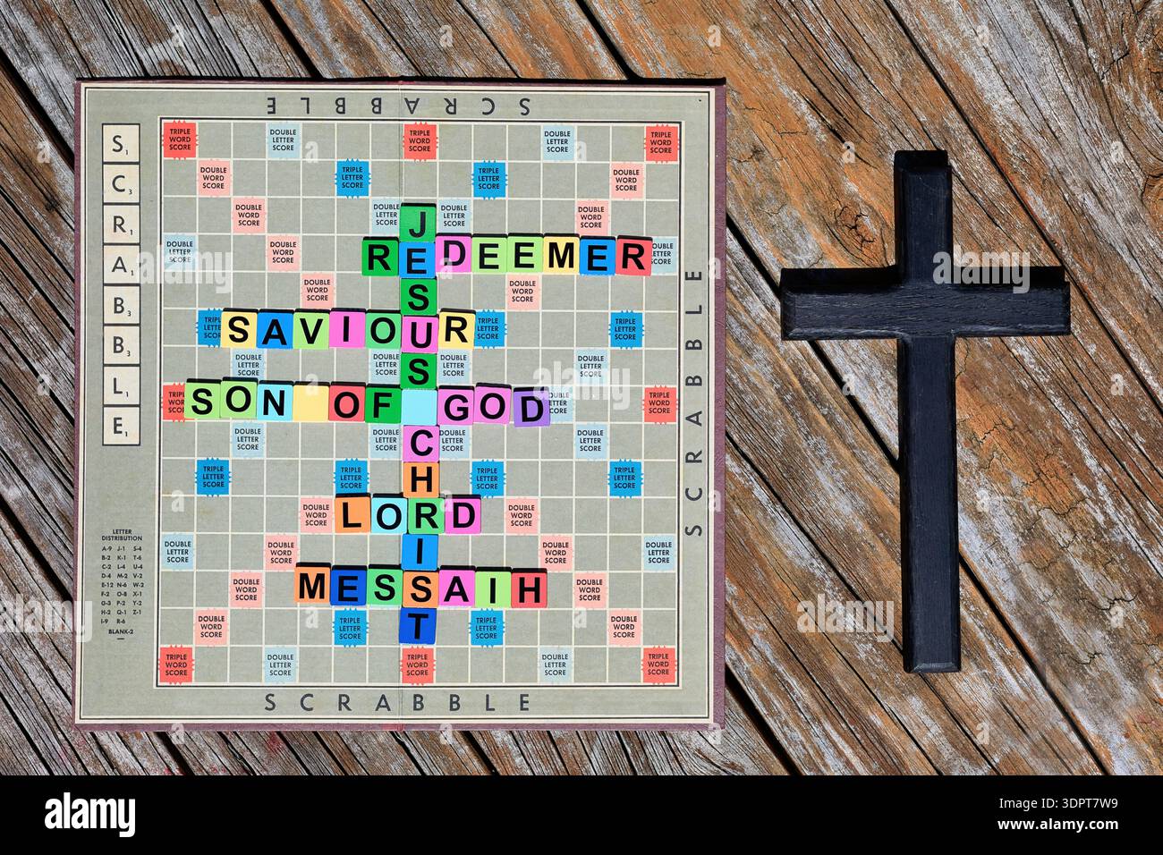 Tabellone di gioco Scrabble con nomi e titoli di Gesù sul tabellone. E una croce di legno nera scura sulla destra. Foto Stock