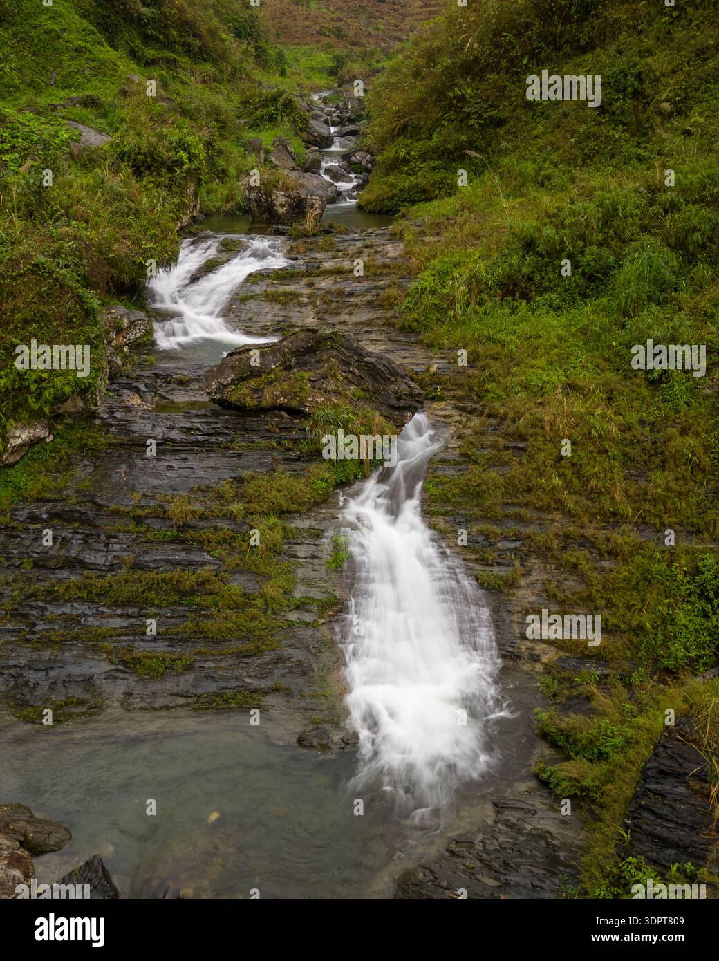 Una vista aerea della cascata di Du Gia che scorre su formazioni rocciose a strati e che si getta in piccole piscine circondate da una lussureggiante vegetazione verde. Foto Stock