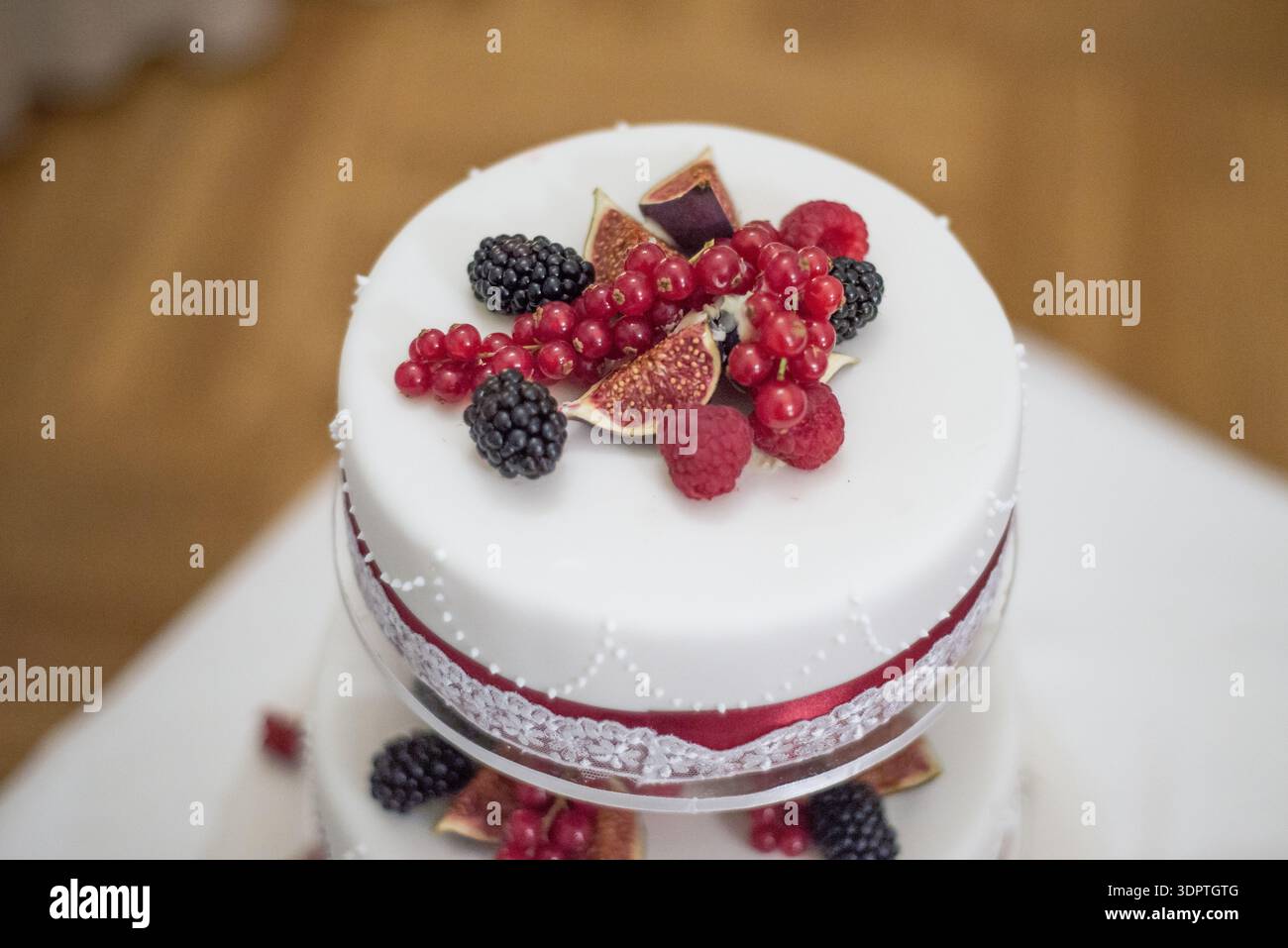 Primo piano di un'elegante torta nuziale bianca decorata con frutti di bosco e fichi freschi. Raffinato design per dessert, ideale per matrimoni, feste, catering Foto Stock