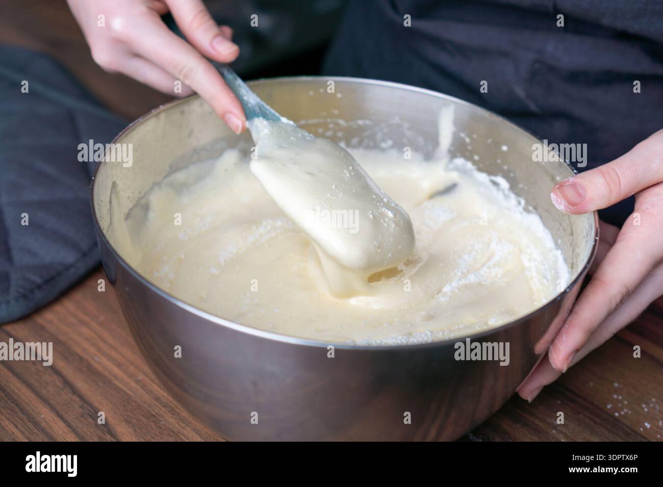 Primo piano di mani mescolando impasti spessi con una spatola in silicone in un recipiente di miscelazione in metallo. Foto Stock