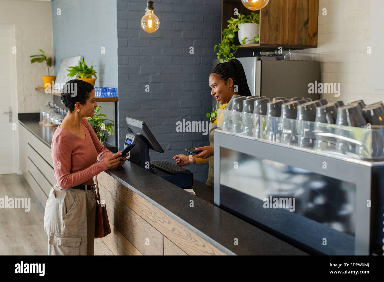 Cliente donna e barista diverse che effettuano il pagamento al bancone del bar utilizzando lo smartphone e registrarsi Foto Stock