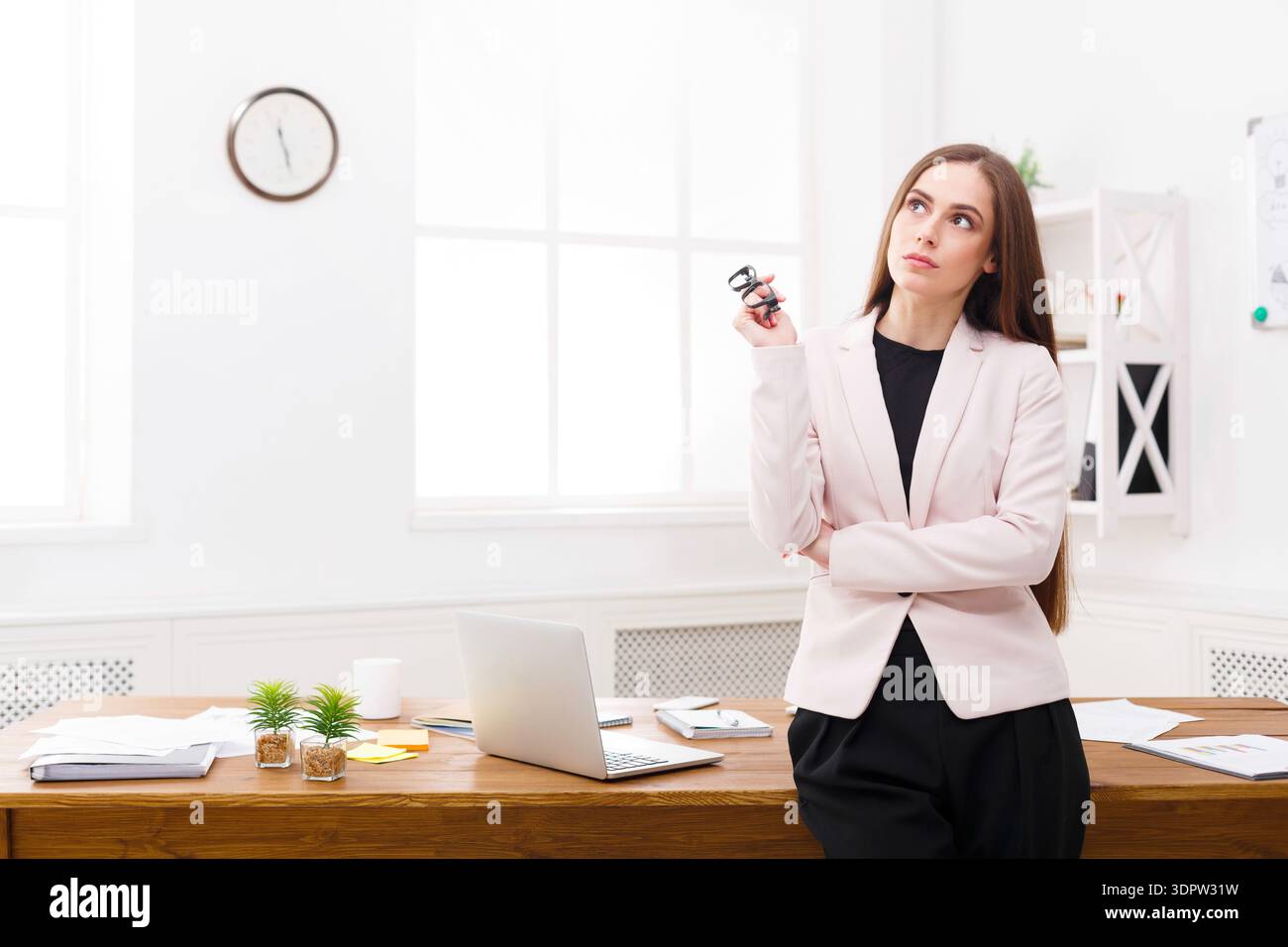 Donna professionista che pensa in un ambiente ufficio con un notebook e documenti sulla scrivania Foto Stock