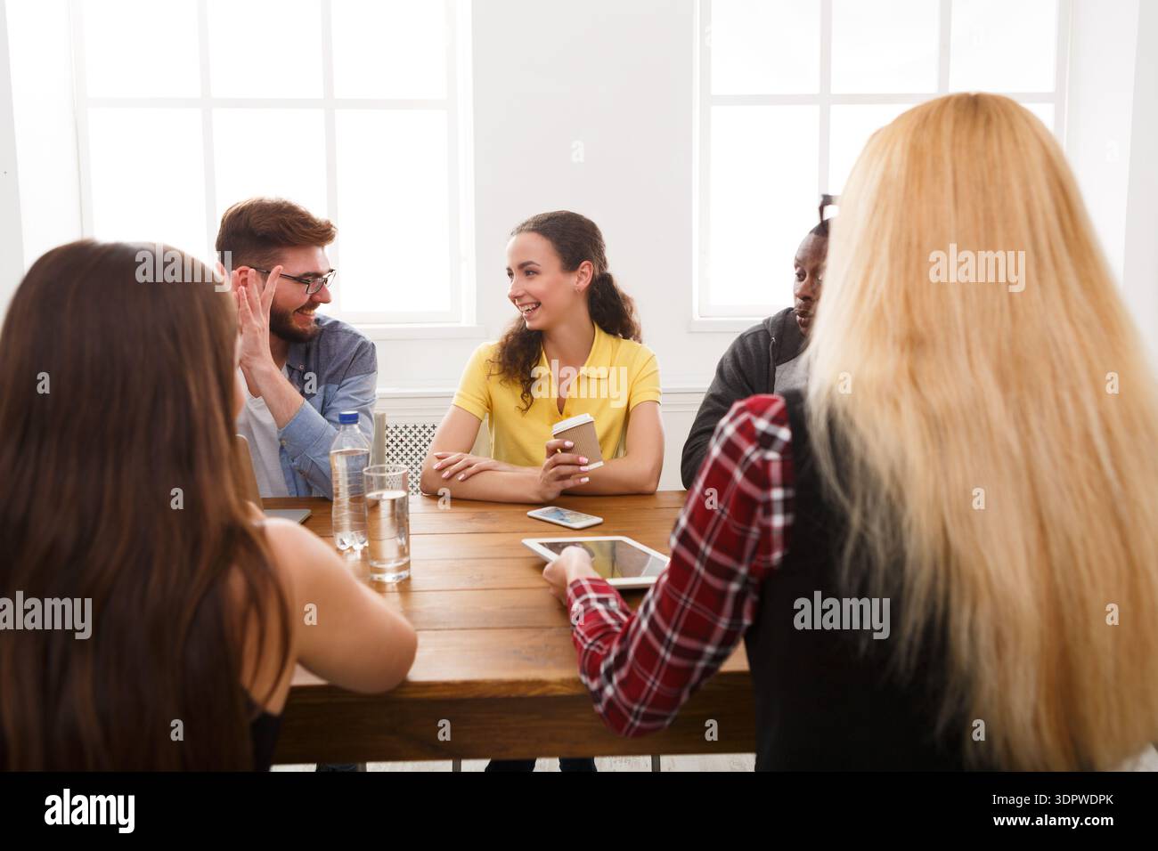 Gruppo di persone che parlano e condividono idee in una stanza luminosa con grandi finestre Foto Stock