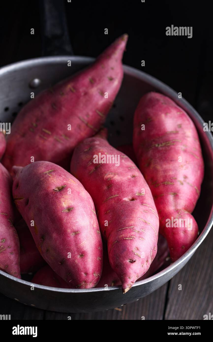 Patate dolci fresche nel recipiente su una superficie scura. Ingredienti vegetali sani e naturali Foto Stock