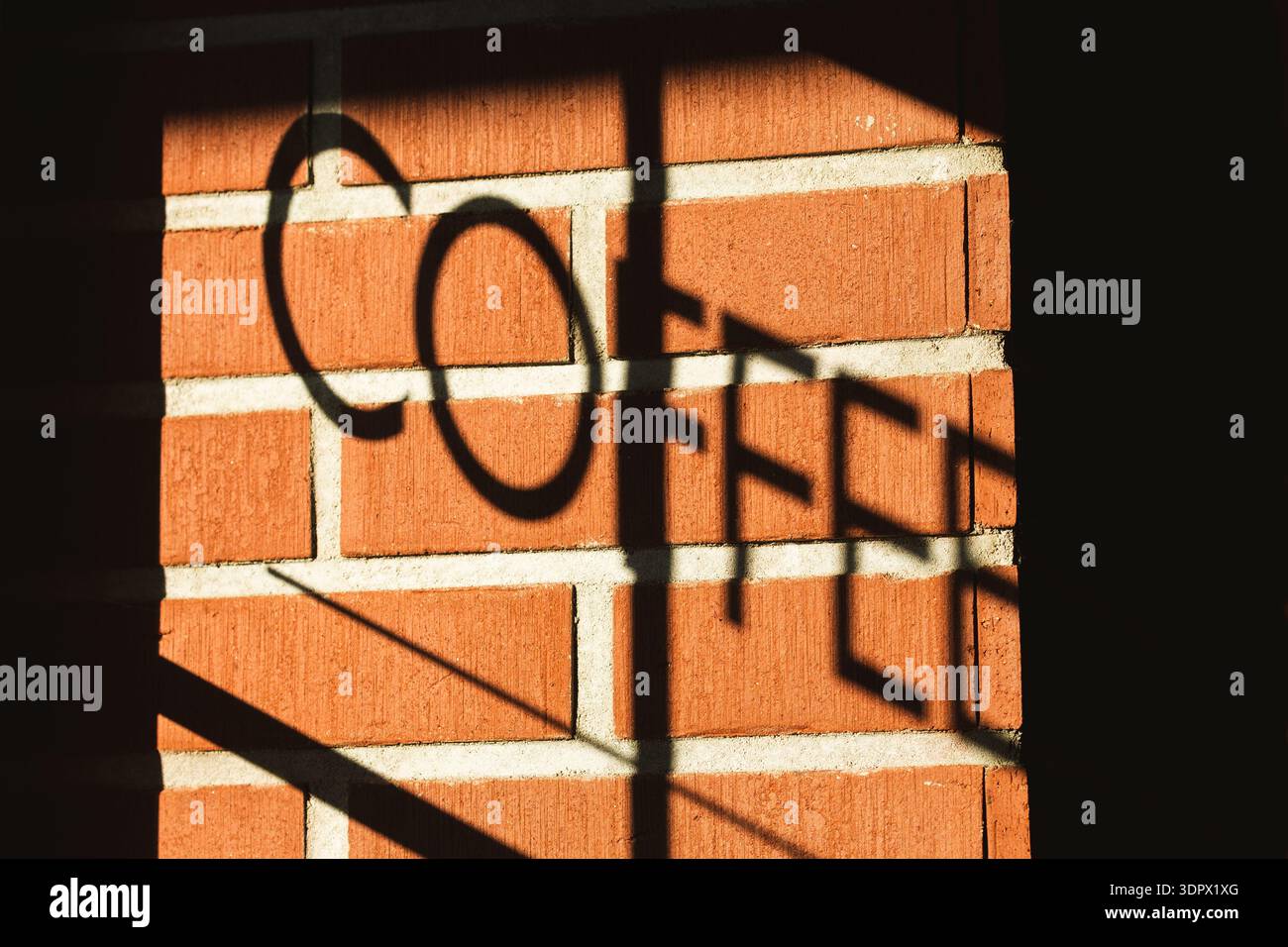 Ombra di un segnale DI CAFFÈ proiettato su una parete di mattoni rossi alla luce calda del sole, creando audaci motivi tipografici e geometrici Foto Stock