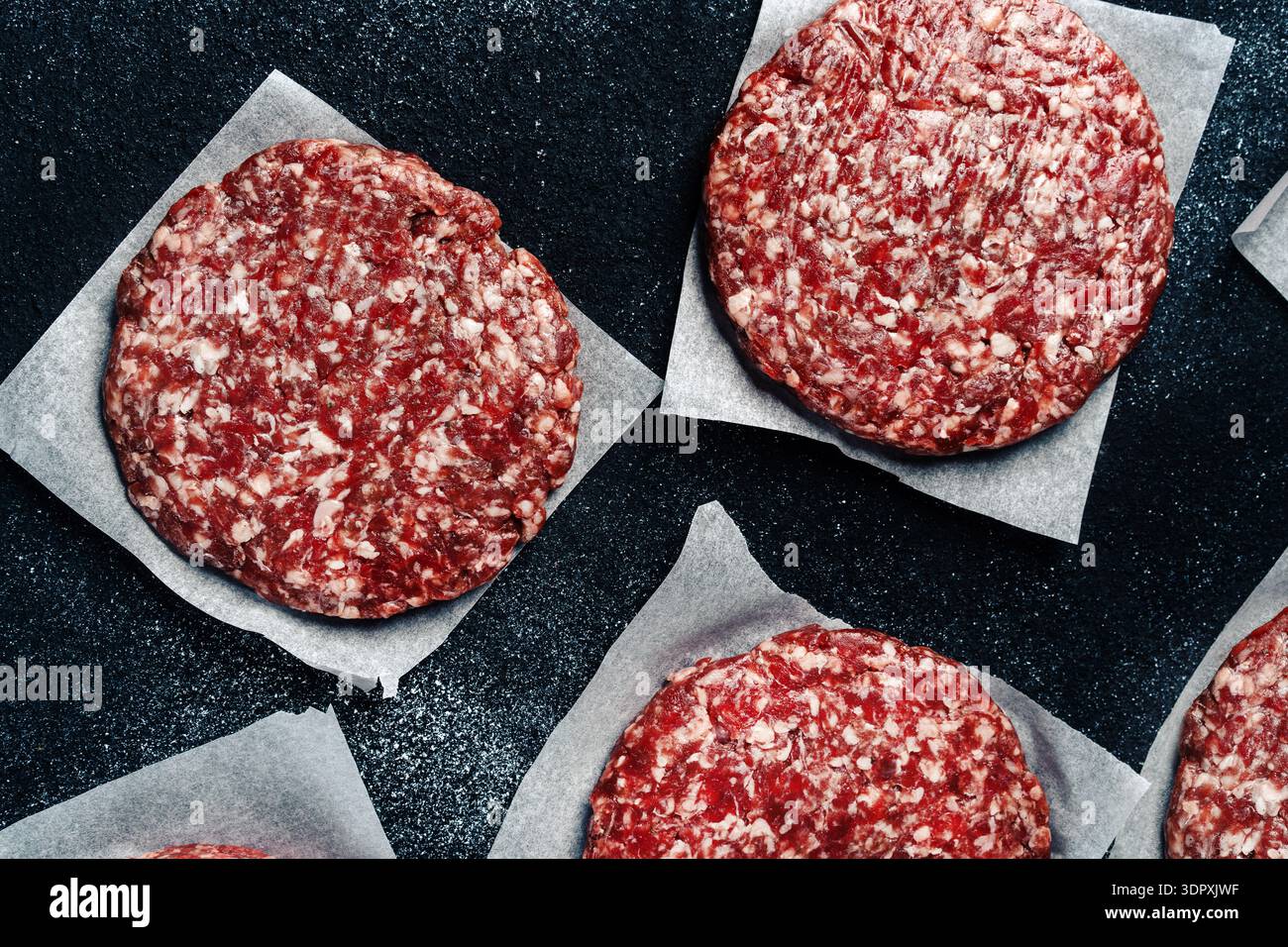 Immagine ravvicinata di hamburger di vitello fresco su carta pergamena, pronto per la cottura alla griglia. La consistenza marmorizzata del vitello migliora il sapore, perfetto per i buongustai Foto Stock