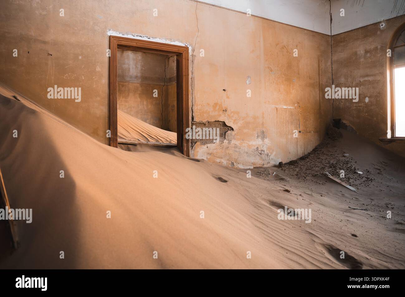 Le dune di sabbia illuminate dal sole riempiono un interno abbandonato nella città fantasma di Luderitz, mostrando l'affascinante miscela di architettura e natura nel deserto del Namib Foto Stock