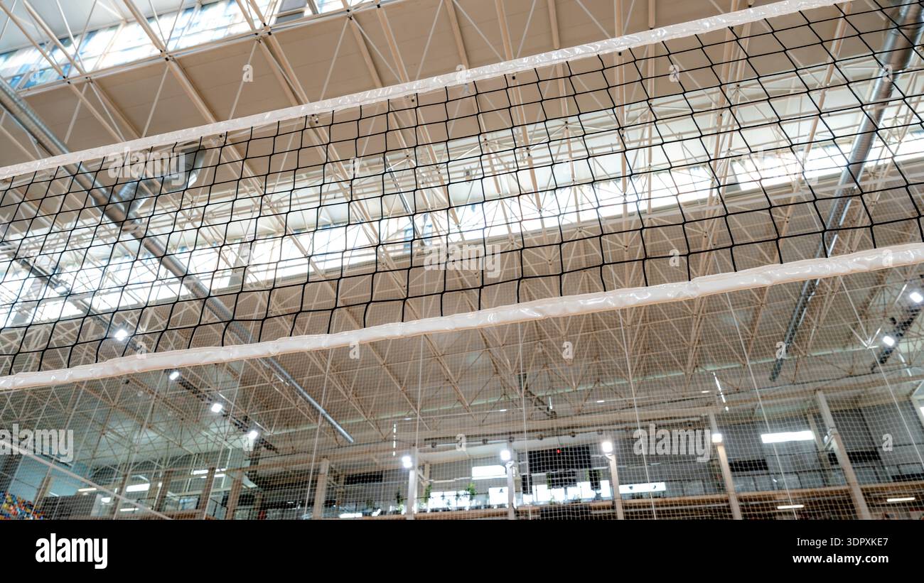 Una prospettiva ravvicinata di una rete da pallavolo che si estende su una palestra interna, con un design geometrico del soffitto splendidamente strutturato che fornisce un Foto Stock