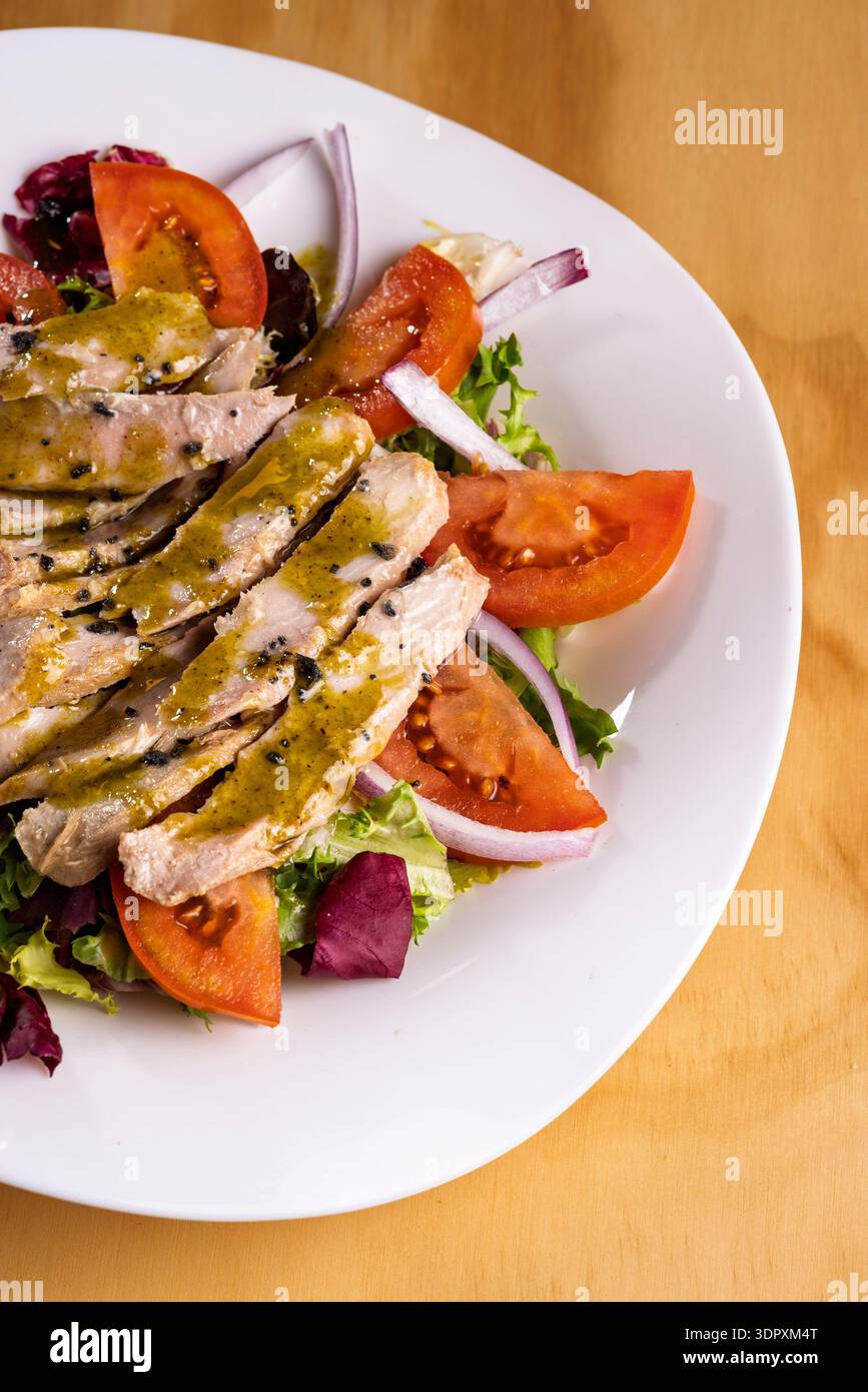 Un delizioso piatto di insalata di pancia di tonno con pomodori ciliegini freschi, cipolla rossa croccante e basilico aromatico, il tutto condito con miele dolce e pistacchio Foto Stock