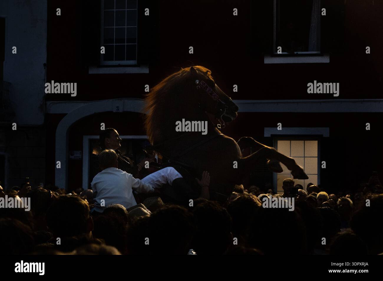 Es Castell, Spagna - 24 luglio 2025: Veduta di un cavallo in mezzo a una folla, la sua silhouette si scontra con l'abbraccio della sera. Foto Stock