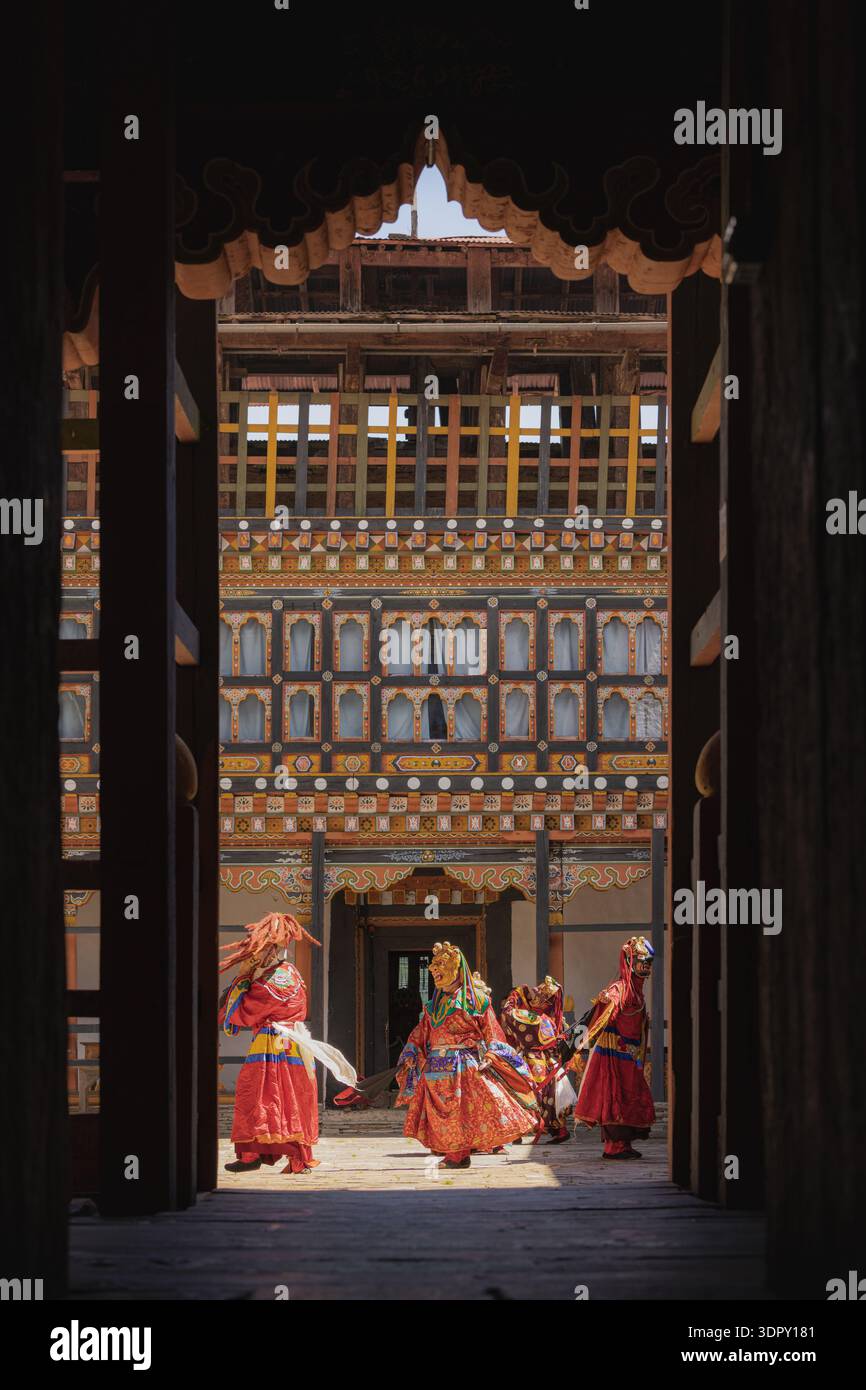 Jakar Dzong, Bhutan - 24 settembre 2025: Veduta di ballerini vibranti in tradizionali costumi rossi, le loro maschere ornate un caleidoscopio di colore contro la t Foto Stock