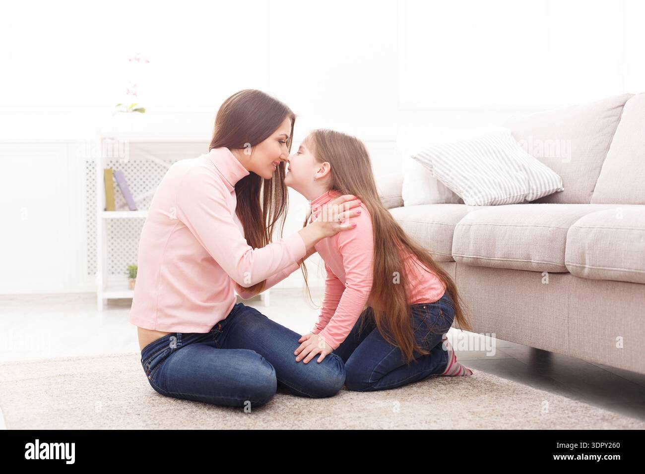 Madre e figlia condividono un momento a casa con espressioni gioiose e una stretta interazione Foto Stock
