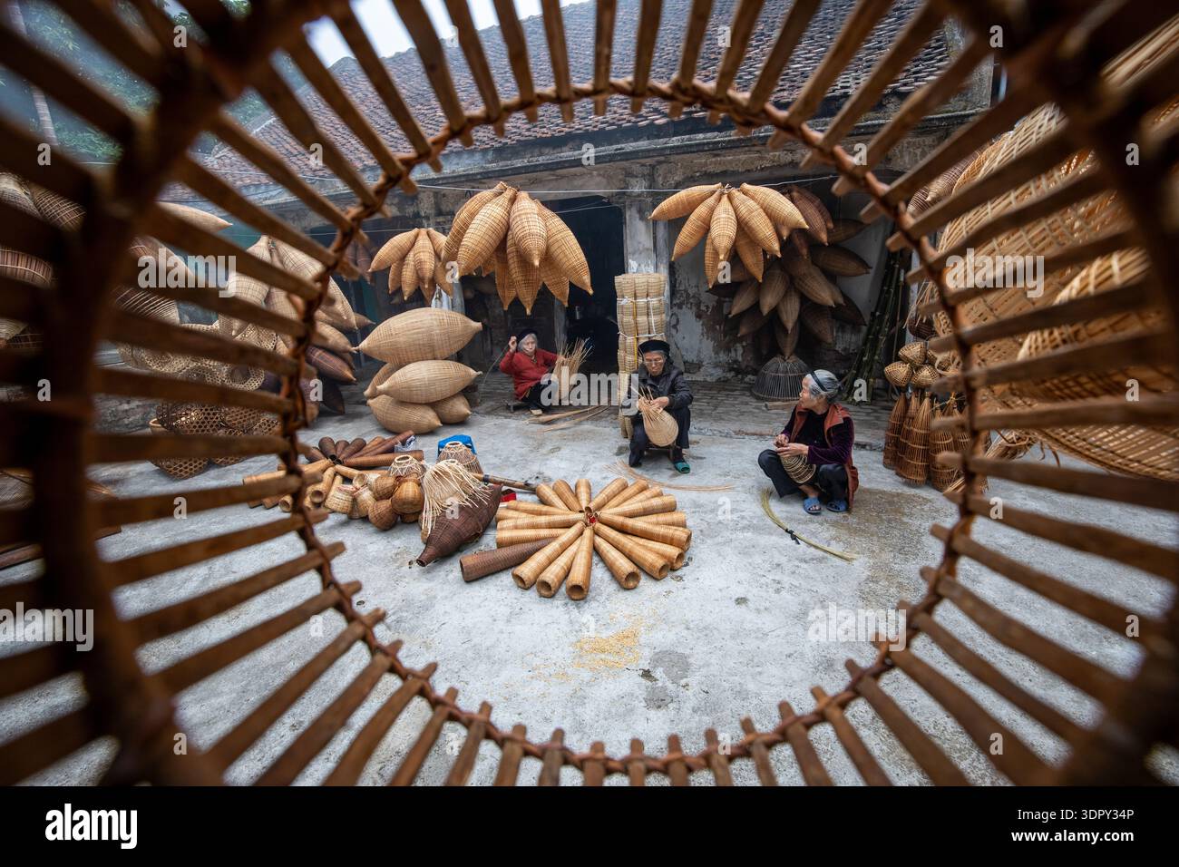 Hưng Yên, Vietnam - 15 dicembre 2019: Veduta degli artigiani che realizzano trappole di bambù sotto le grondaie, le tonalità calde contrastano con il grigio freddo del fiume Foto Stock