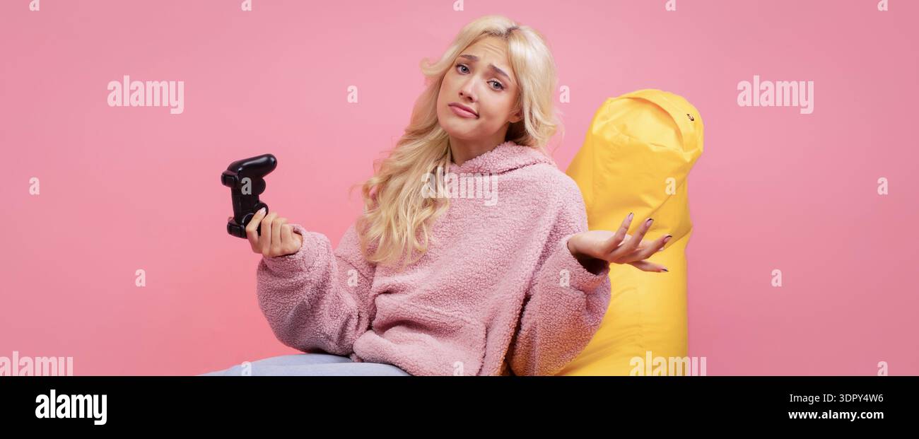 Una giovane donna siede con il controller di gioco in Colorful Room mentre sembra confusa sul gioco Foto Stock