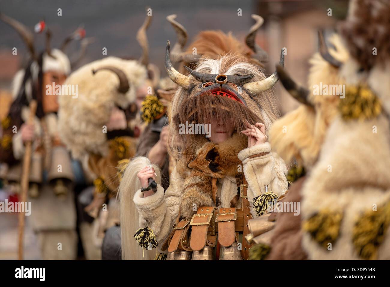 Novi Iskar, Bulgaria, 15 febbraio 2026: Kukeri in costumi tradizionali in pelle con grandi campane rituali e maschere in legno intagliato si esibiscono al Surva Festi Foto Stock