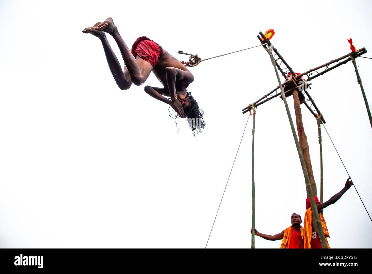 Sylhet, Bangladesh - 14 aprile 2025: Vista di un uomo audace sospeso a mezz'aria, che esegue un'emozionante acrobazia contro il cielo bianco, con gli spettatori i Foto Stock