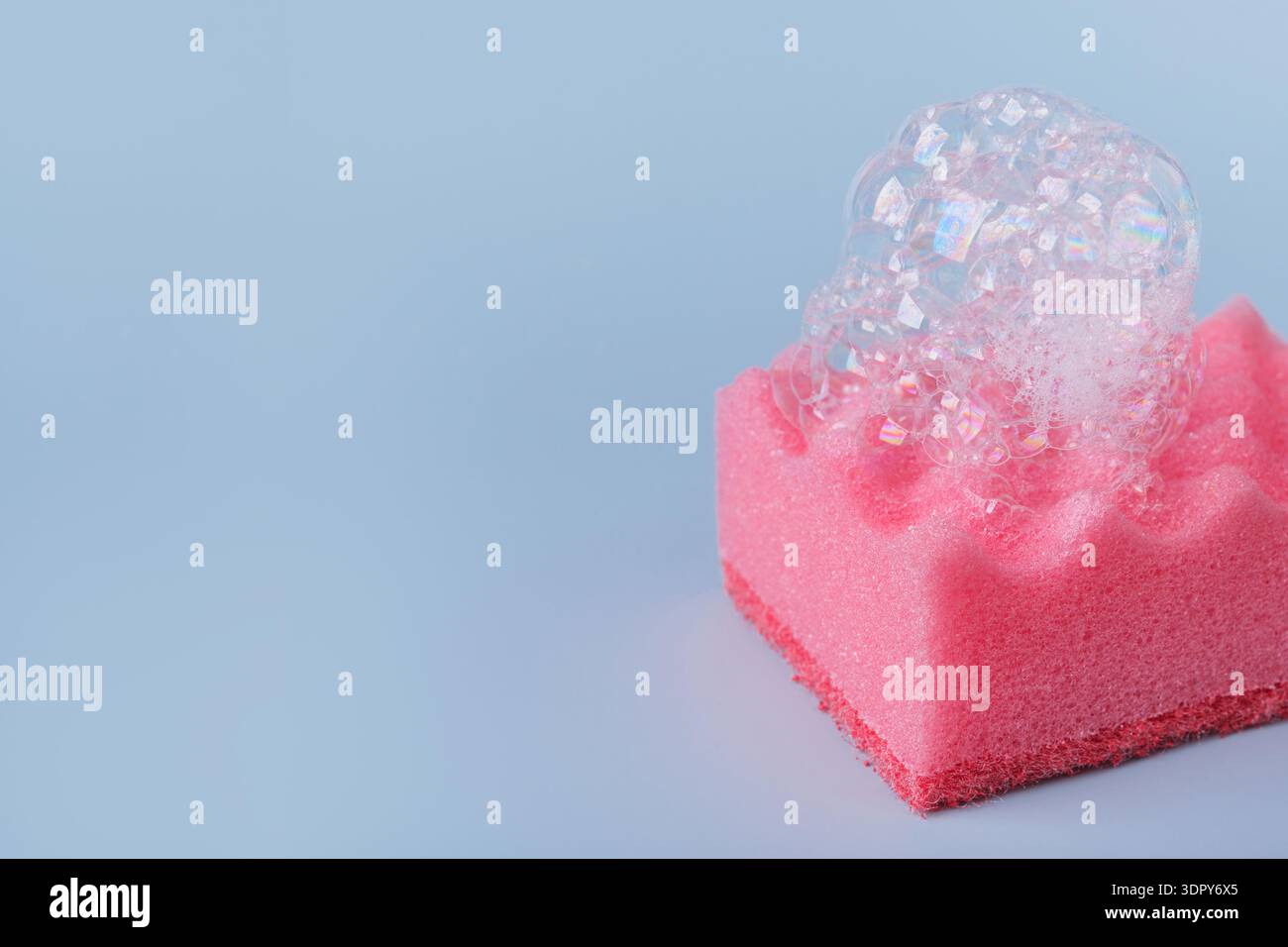 Spugna rosa con schiuma di sapone su sfondo blu Foto Stock