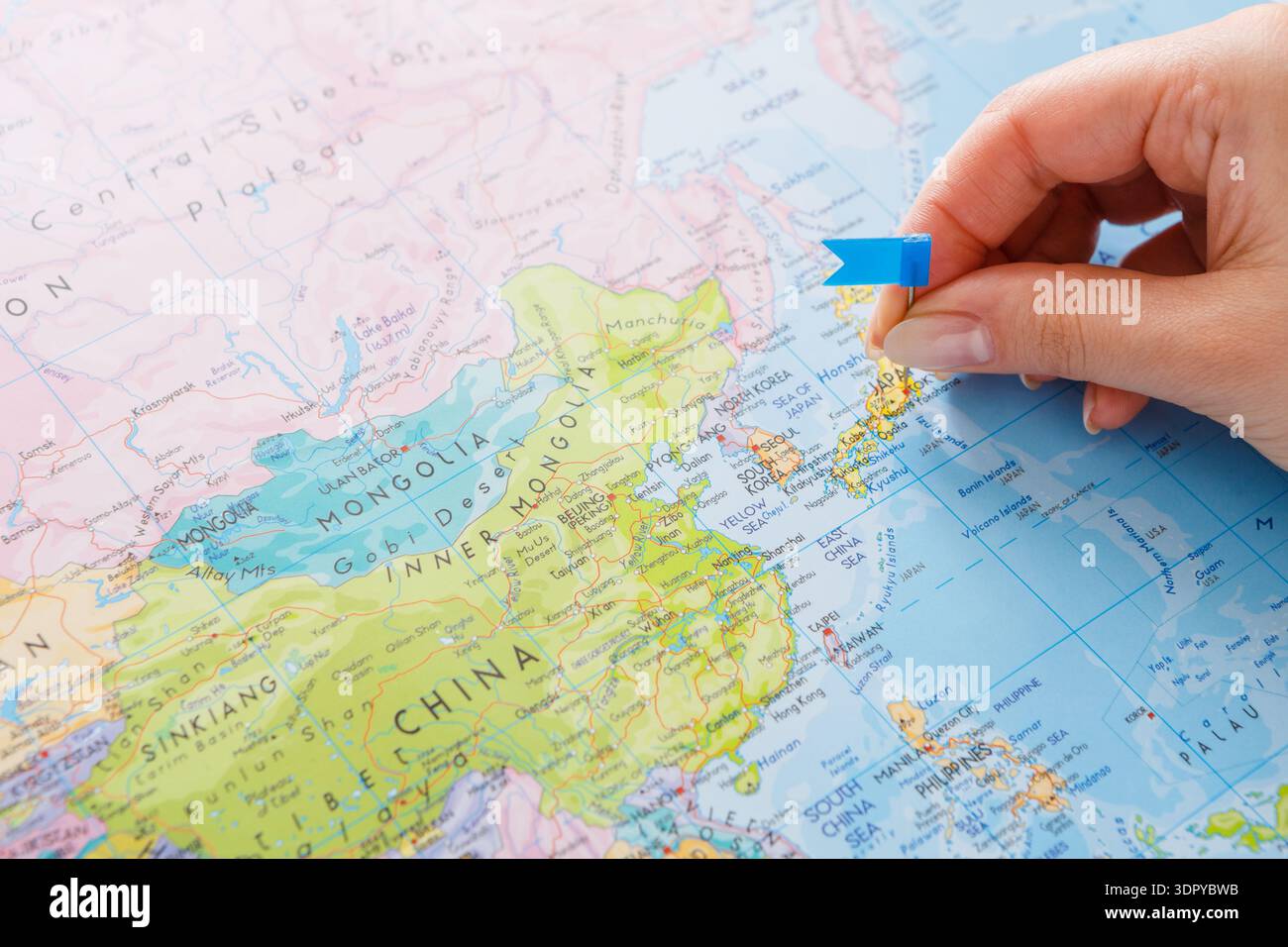 Scegliere una posizione su una mappa dell'Asia con una bandiera blu in mano Foto Stock