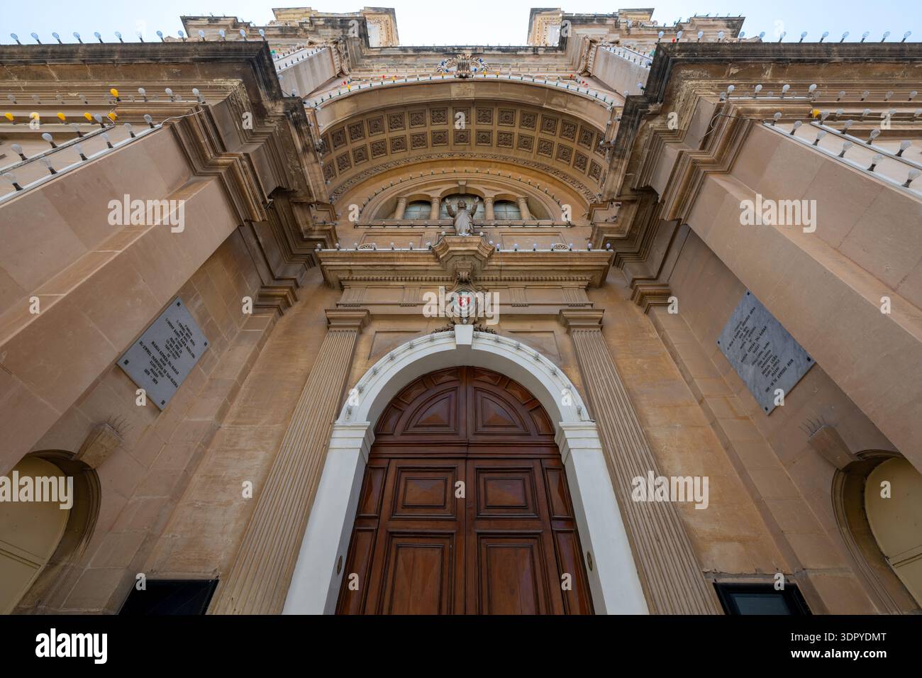 Vista dall'angolo basso della facciata della Chiesa Arcivescovile Stella Maris a Sliema, caratterizzata da una grande porta in legno, pilastri in pietra e soffitto portico ad arco Foto Stock