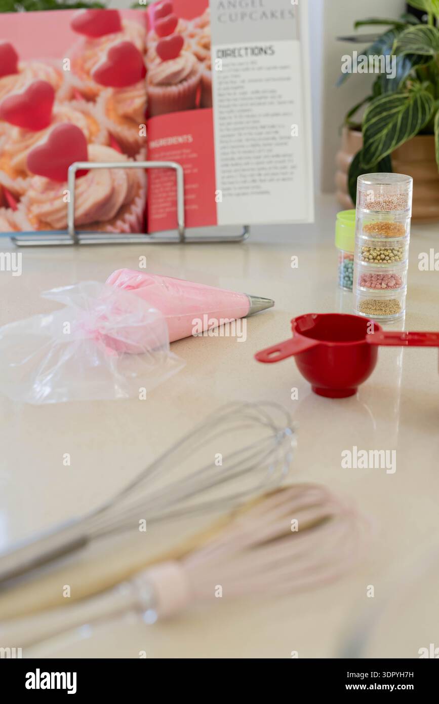 Il sacchetto per tubazioni pieno di glassa rosa è posizionato sul piano di lavoro con frusta, dosatore e spruzzette Foto Stock