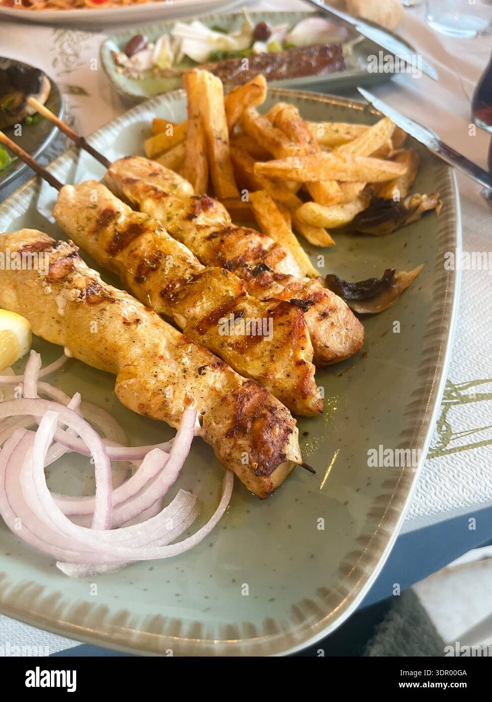 Spiedini tradizionali greci di pollo con souvlaki serviti con patatine fritte croccanti, cipolla e limone su un piatto. - Immagine stock catturata con smartphone