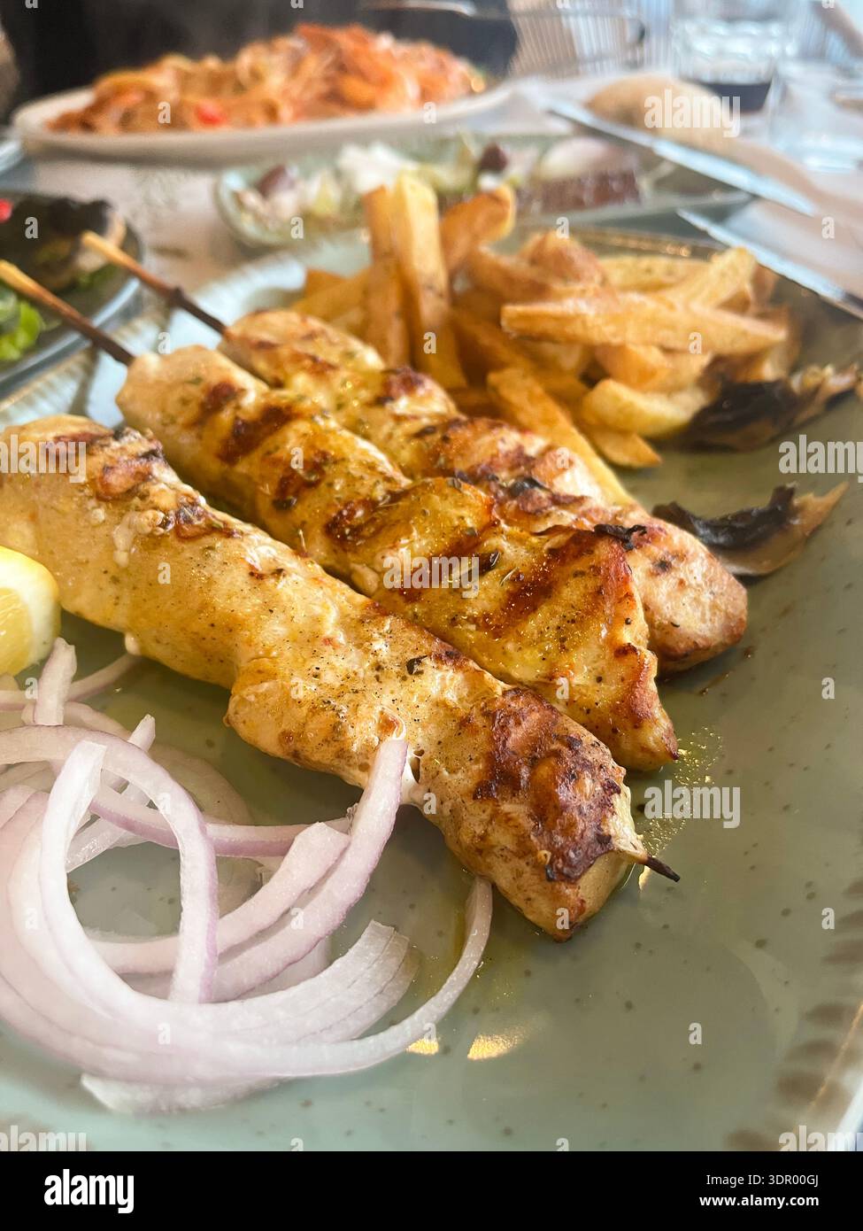 Spiedini tradizionali greci di pollo con souvlaki serviti con patatine fritte croccanti, cipolla e limone su un piatto. - Immagine stock catturata con smartphone