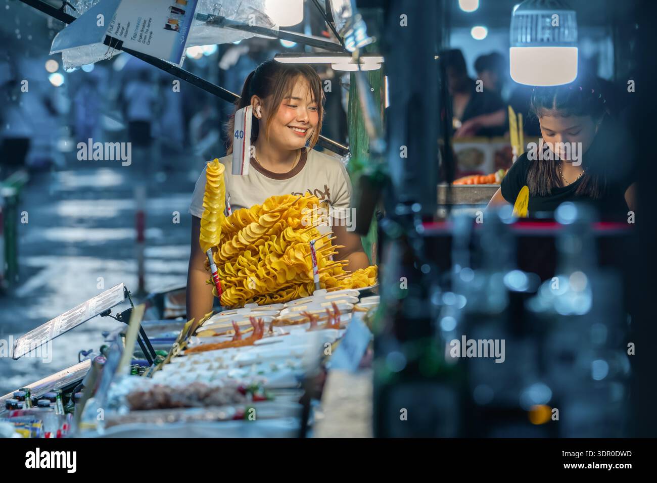 Khaolak Thailand 17 11 2025: In un vivace mercato notturno in Thailandia, i venditori servono fast food mentre cade la pioggia. I clienti curiosano tra le bancarelle alimentari e assaggiano Foto Stock