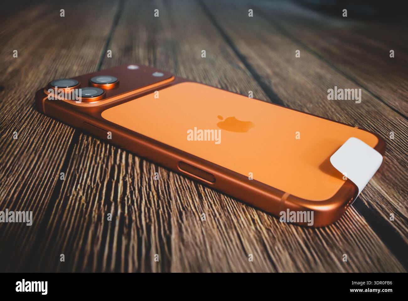 IPhone 17 Pro Max in arancione cosmico si trova su un tavolo in legno, con una profondità di campo ridotta che illustra il suo design elegante e il sistema di fotocamera a triplo obiettivo Foto Stock