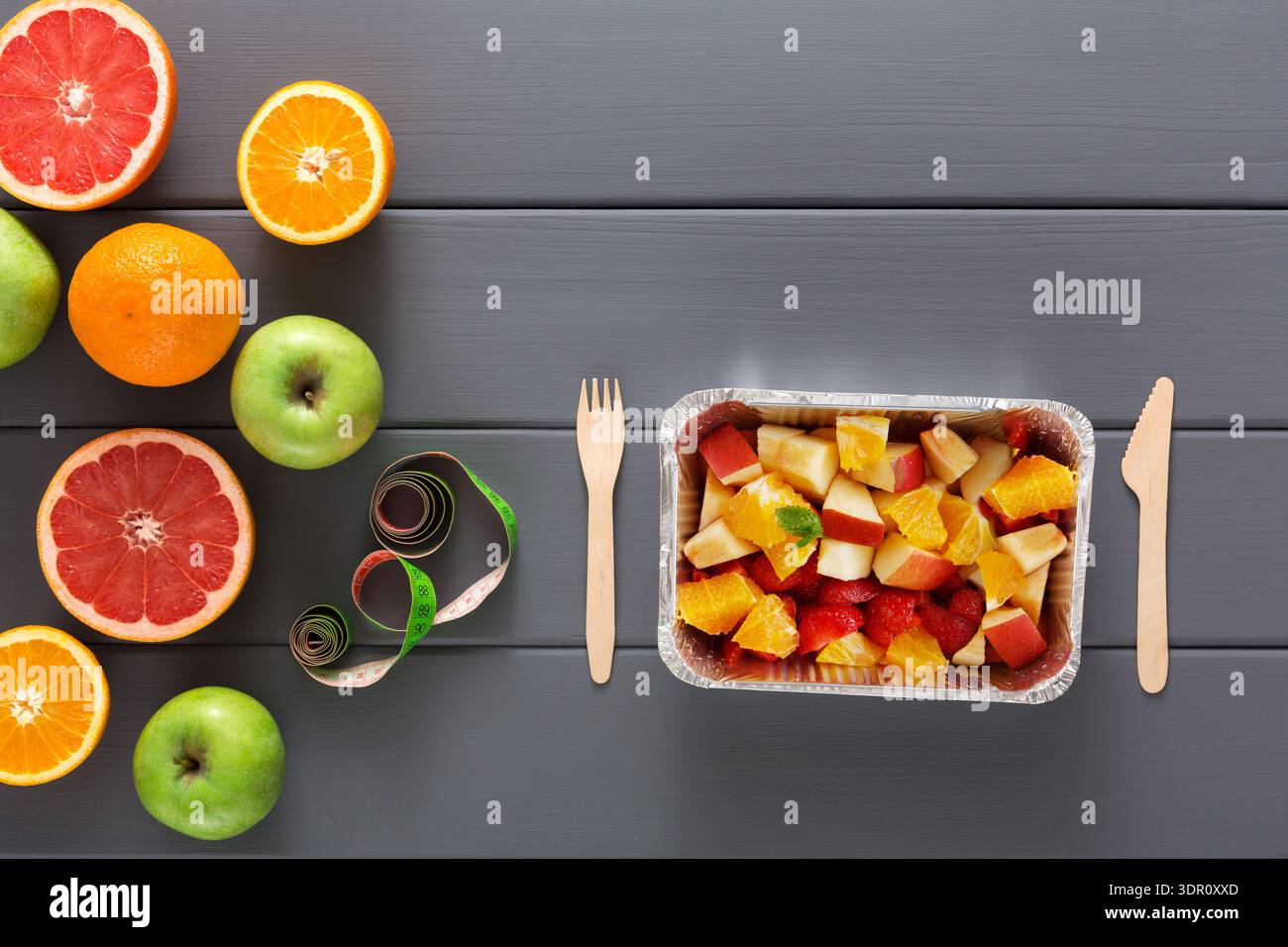Vassoio di frutta con frutta mista e posate disposte su un piano grigio Foto Stock
