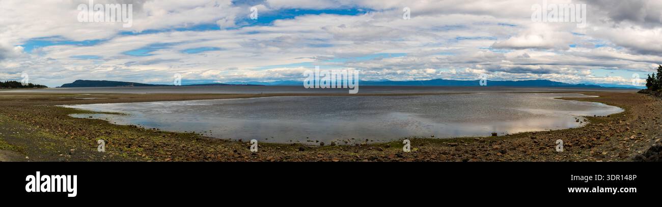 Un'ampia scena panoramica mostra una costa rocciosa, montagne lontane e un cielo per lo più nuvoloso lungo l'isola di Vancouver. Foto Stock