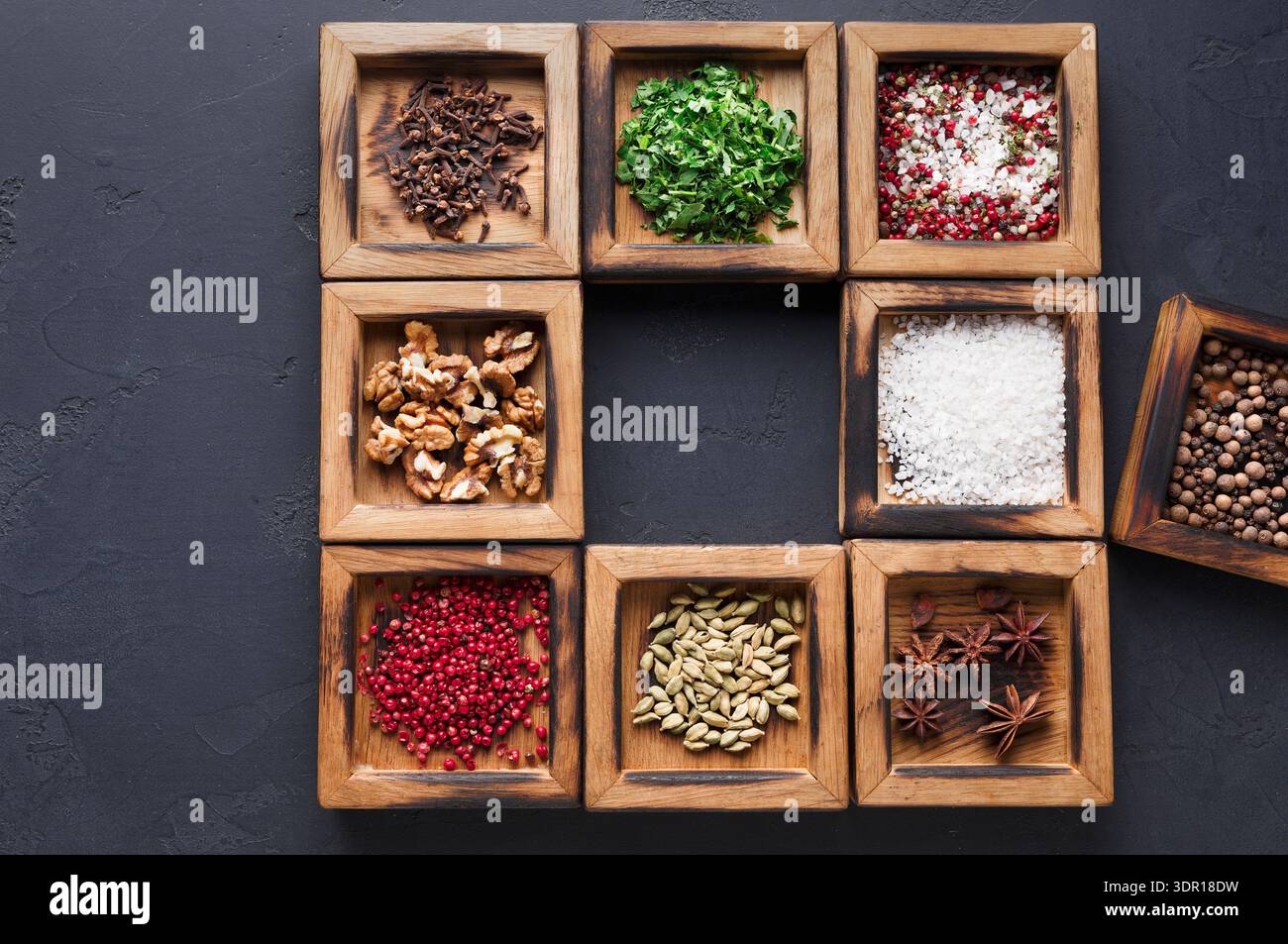 Varietà di spezie ed erbe disposte in contenitori di legno su una superficie scura Foto Stock