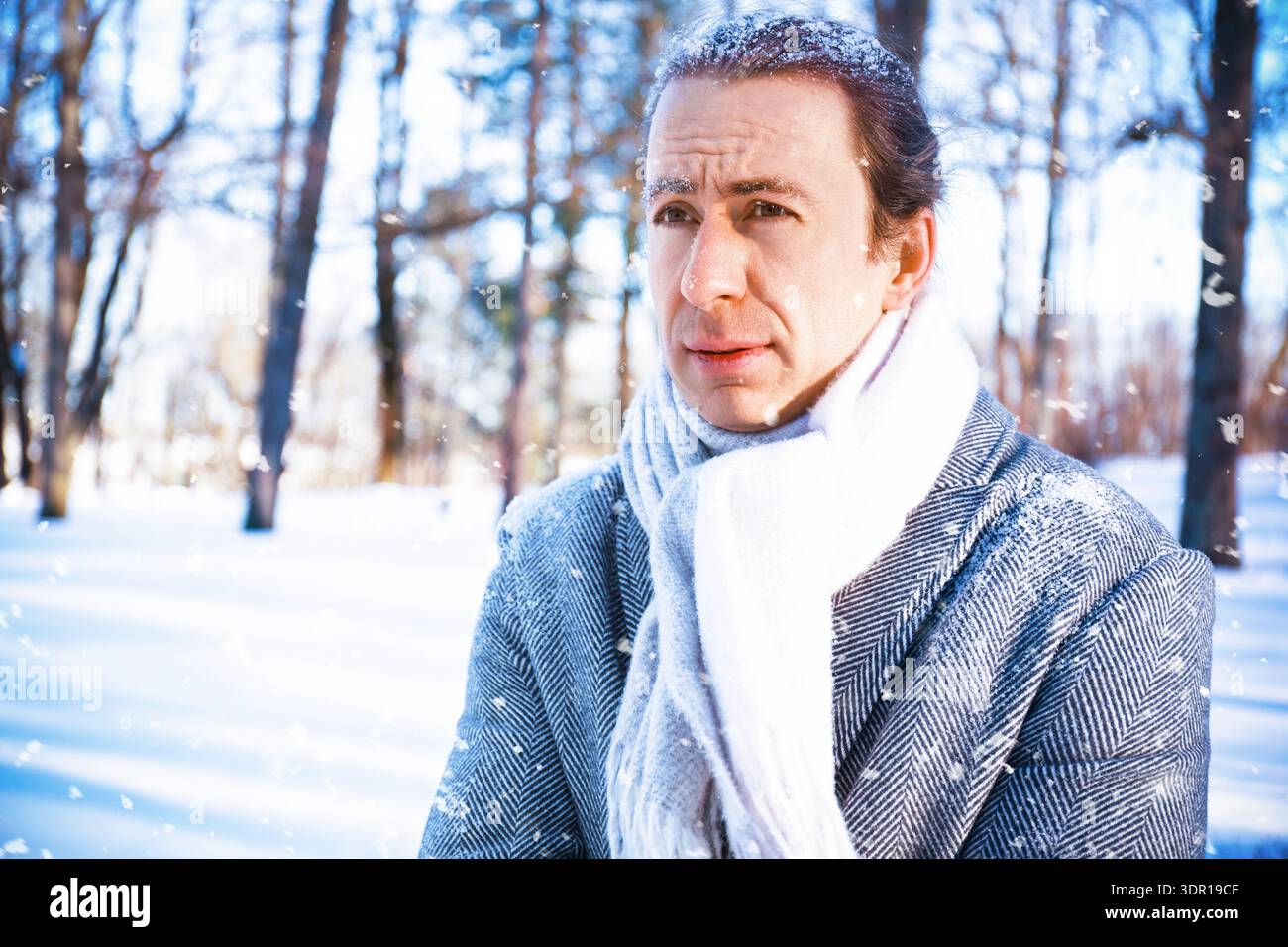 Un ritratto di un uomo congelato in un parco innevato. Appare congelato e pensivo, con la neve nei capelli, durante una tempesta di neve soleggiata. Concettualmente, IT Foto Stock